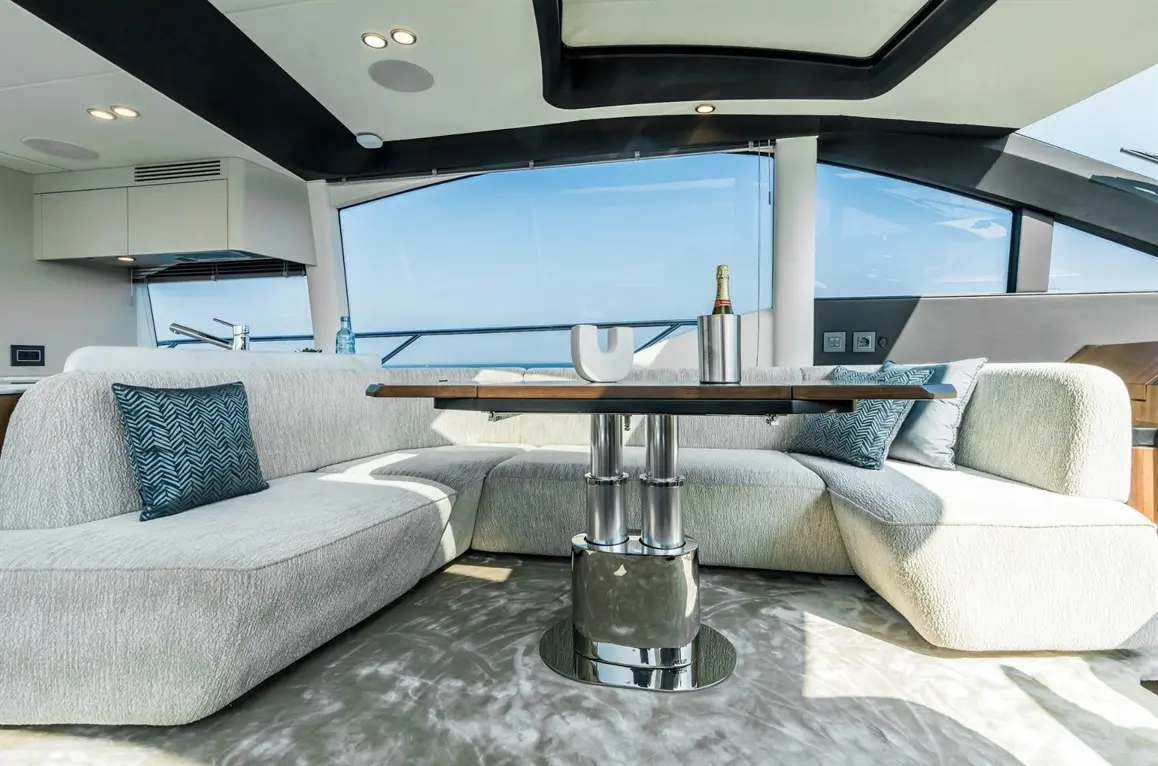 Luxurious yacht interior featuring a grey lounge area, wooden table, champagne in an ice bucket, and panoramic sea views.